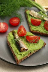 Delicious sandwiches with sprats, tomatoes, avocado puree and dill on table, closeup