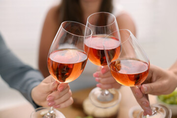 People clinking glasses with rose wine indoors, closeup