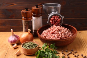 Manual meat grinder with beef mince, spices and parsley on wooden table