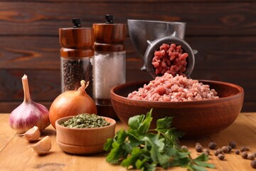 Manual meat grinder with beef mince, spices and parsley on wooden table