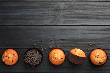 Delicious freshly baked muffins with chocolate chips on dark gray table, flat lay. Space for text