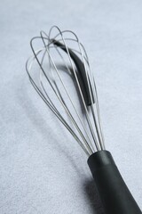 Metal whisk on gray table, closeup. Kitchen tool