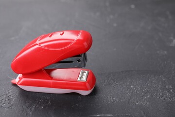 Red stapler on black textured table, space for text