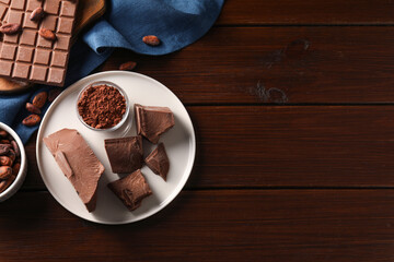 Pieces of tasty milk chocolate, cocoa beans and powder on wooden table, flat lay. Space for text