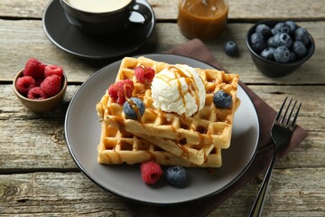 Delicious Belgian waffles with ice cream, berries and caramel sauce on wooden table