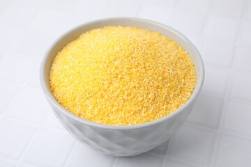 Raw cornmeal in bowl on white tiled table, closeup