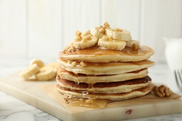 Fototapeta na wymiar Delicious pancakes with bananas, walnuts and honey on white marble table, closeup