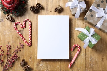 Flat lay composition with blank paper sheet, candy canes and Christmas decor on wooden table, space for text. Letter to Santa