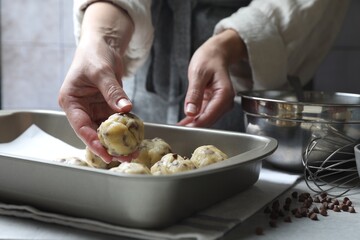 Woman putting raw chocolate chip cookie ball on baking pan at table, closeup
