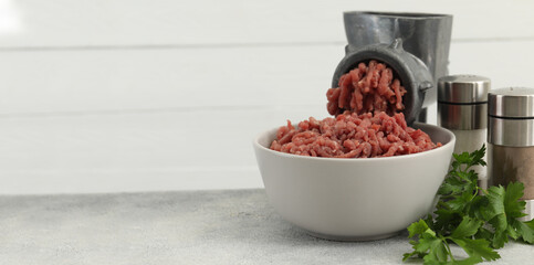 Manual meat grinder with beef mince, spices and parsley on grey table. Banner design with space for...