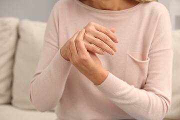 Mature woman suffering from pain in hand indoors, closeup. Rheumatism symptom