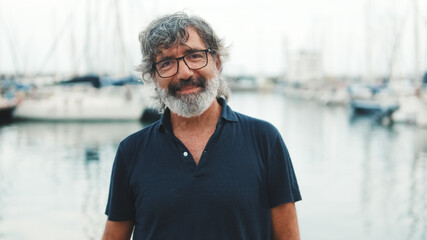 Close-up of happy senior man in glasses standing in port and looking at camera on yachts background