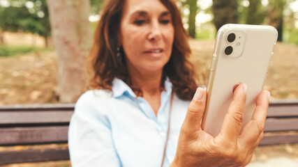 Close-up of an elderly woman's hands using phone while sitting in park, background blurred
