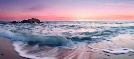 Obraz premium The colorful sunset is seen from the blue, pink sea beach with the waves gently flowing onto the shore