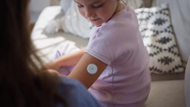 Nurse applying a continuous glucose monitor sensor to the arm of a diabetic girl.