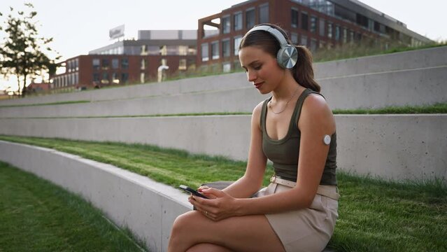 Diabetic woman sitting outdoors, watching social media content on smart phone.