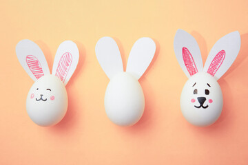 Happy Easter. Food photo. Chicken eggs with cute bunny faces and rabbit ears on pastel beige...
