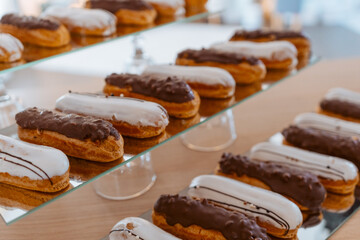 Eclairs with white and chocolate icing are laid out in a row on a mirror surface, display in a store.