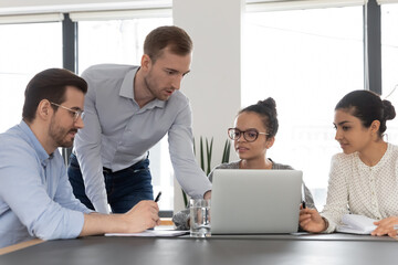 Multiracial businesspeople sit at desk in boardroom look at laptop screen brainstorming over project together. Multiethnic diverse employees cooperate using computer, involved in team discussion.