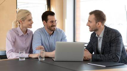 Smiling male relator or broker talk consult happy young Caucasian couple at meeting in office. Man real estate agent have consultation with excited millennial family buyers. Rent, realty concept.