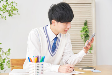 自宅でスマートフォンを使って勉強する男子高校生