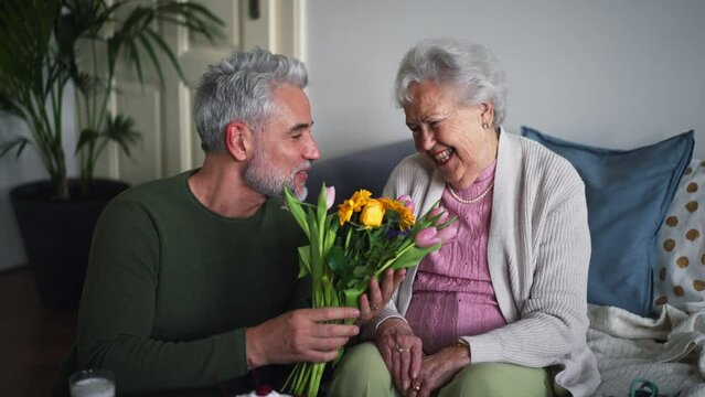 Mature man celebrating with his senior mother at her apartment.