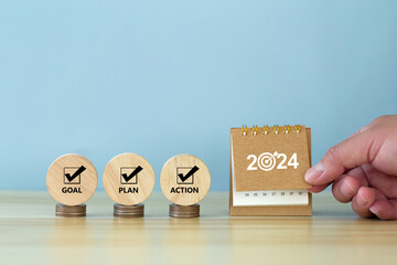 Happy New Year 2024 banner background. 2024 numbers year with target dart icon on desk calendar with hand turns over a calendar sheet.  Goal, Plan, Action on wooden cube. Business goals plan action. - obrazy, fototapety, plakaty