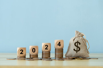 Happy New Year 2024. Text 2024 on a wooden cube on coins stacked with a sack idea for Budget....