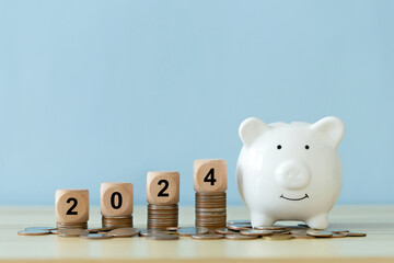 Happy New Year 2024. Text 2024 on a wooden cube on coins stacked with a piggy bank idea for savings. target business cost and budget planning for the new year. Budget, investment, and financial.