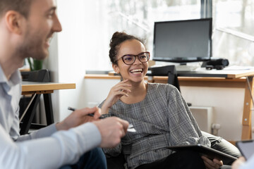 Smiling young African American woman employee have fun talking brainstorming with diverse...