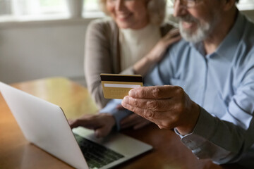 Seniors and ecommerce. Close up cropped shot of mature married couple using payment card for online shopping booking hotel ordering prepaid services. Aged ebank customers pay fee from home computer