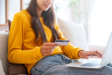 Young asian woman sitting on sofa in living room, makes online banking payments through the...