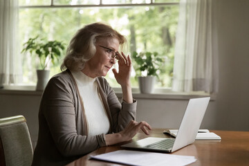 Modern day retiree. Pensive aged female pensioner work by laptop computer from home study at web course in third age university on distance. Focused adult woman in glasses search data online using pc