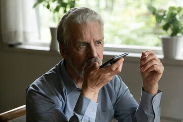 Elderly and tech innovations. Confident middle aged man dictate voicemail message using mobile...