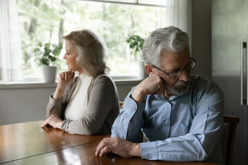 Disagreement between elderly spouses. Stressed upset senior husband wife sit at table separately...