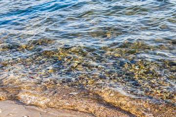 Background of sandy, stones and flowing waves on the sea beach. Summer holidays concept