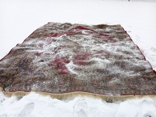 A red carpet is lying on the street in the snow. Cleaning carpets in winter.
