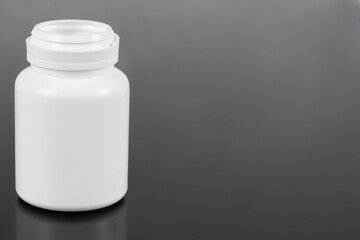 White plastic bottle for pills isolated on a dark background. White container on a black background. Copy space