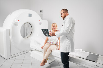 Medical computed tomography or MRI scanner. Doctor holding and explaining results of MRI. Woman patient after MRI, sitting on couchette. Concept of medicine, healthcare and modern diagnostics. - obrazy, fototapety, plakaty
