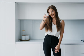 Cheerful girl  rising cup of pure water toothy smiles standing at kitchen home. Ecology concept,...