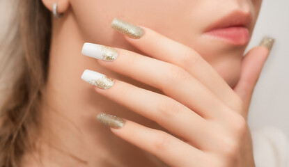 Female hands with long nails with glitter nail polish. Long gold nails near face. Stylish fashion manicure. - obrazy, fototapety, plakaty