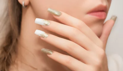 Tuinposter Female hands with long nails with glitter nail polish. Long gold nails near face. Stylish fashion manicure. © devmarya