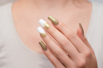 Female hands with long nails with glitter nail polish. Long gold nail design. Women hand with...