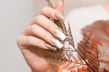 Female hands with long nails with glitter nail polish. Long gold nail design. Women hand with...