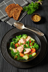 salmon, veggies and green herbs soup in bowl