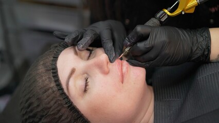 Permanent makeup. The master makes a lip tattoo for a client in a beauty salon. Young woman...