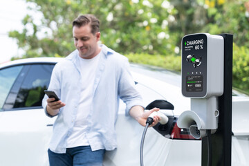 Modern eco-friendly man recharging electric vehicle from EV charging station, using Innovative EV...