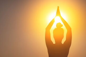 woman meditates at sunset or dawn. Dark female silhouette with folded hands raised above her head, close-up. Light pours overhead