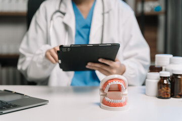 Doctor stomatologist is working on a Tablet computer and tooth model in a modern office in the...