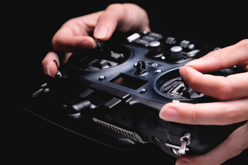 Close-up view of a woman operating the remote control of an FPV racing drone. Hands holding black...